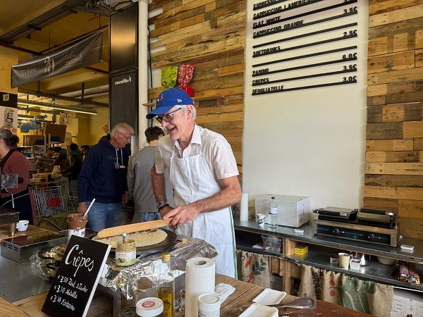 Ein Mann steht hinter einem Tresen und macht Crepes, hinter ihm an der Wand hängt die Preistafel